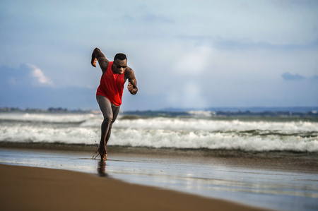 young attractive fit athletic and strong black African American man running at the beach training hard and sprinting on sea water in professional athlete lifestyle and ripped runner workoutの写真素材