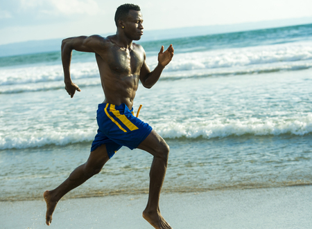 young attractive fit athletic and strong black African American man running at the beach training hard and sprinting on sea water in professional athlete lifestyle and ripped runner workoutの写真素材