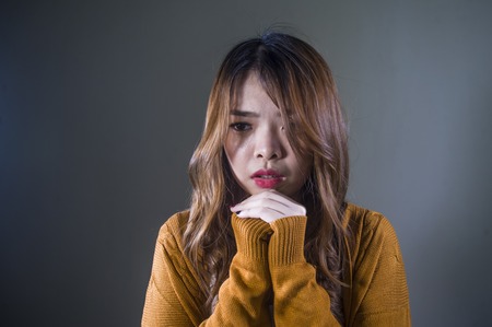 young crazy desperate and sad Asian Korean woman looking depressed and helpless feeling anguish and pain on isolated dark background in pain face expression suffering depressionの写真素材