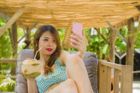 lifestyle portrait of young happy and attractive Chinese student girl at tropical resort garden...
