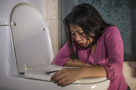 young drunk or pregnant Asian woman vomiting and throwing up in toilet WC feeling unwell and sick suffering stomach ache and nausea as pregnancy symptom or intoxicated in hangoverの写真素材