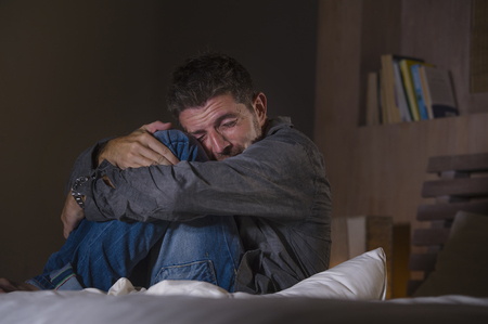 young crazy desperate and depressed man crying on bed suffering anxiety crisis and depression problem feeling overwhelmed and stressed late at night  in fetal position on dramatic lightの写真素材
