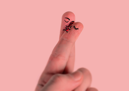 Valentines day greeting card featuring hand with two fingers together painted as man and woman face kissing each other representing happy lovers and romantic couple in love isolated on pinkの写真素材