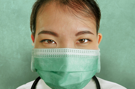 close up isolated portrait of young attractive and confident Asian Chinese medicine doctor woman in protective face mask and scrubs with stethoscope in hospital health care and medical staff conceptの写真素材