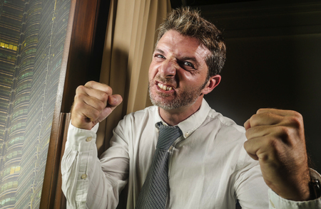 crazy desperate and stressed businessman feeling angry and upset in furious face expression wearing necktie late night in office working at corporate company overwhelmed and frustratedの写真素材