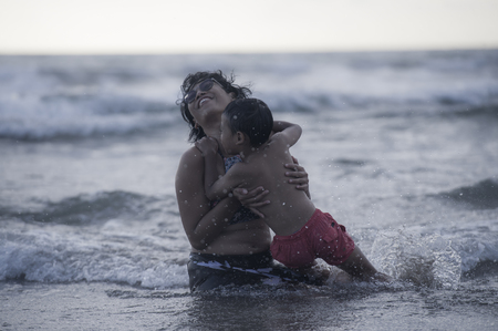 lifestyle candid portrait of young Asian Indonesian mother and little son enjoying summer holidays having a bath on the sea at tropical beach in family vacation trip the kid loving the sea waterの写真素材