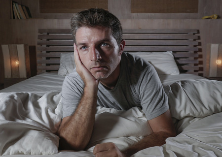 dramatic portrait of young attractive sad and depressed man lying in bed feeling worried suffering depression problem and anxiety crisis thoughtful and pensive awake at night at home bedroomの写真素材