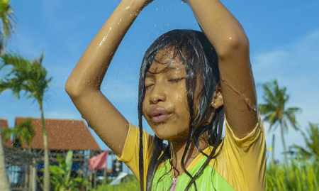 young happy and carefree beautiful child 7 or 8 years old outdoors having shower at a beautiful rice terrace playful under the water wearing cute girl swimsuit enjoying holidays and nature freeの写真素材