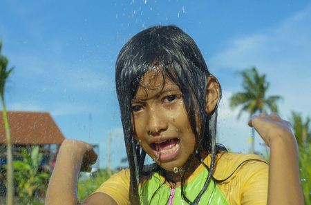 young happy and carefree beautiful child 7 or 8 years old outdoors having shower at a beautiful rice terrace playful under the water wearing cute girl swimsuit enjoying holidays and nature freeの写真素材