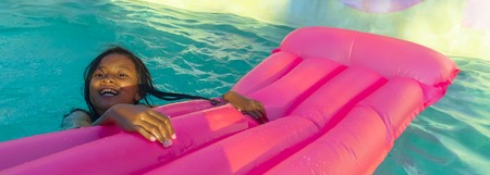 lifestyle outdoors portrait of young happy and cute female child having fun with inflatable airbed in holidays resort swimming pool smiling carefree and cheerful in young girl vacations conceptの写真素材