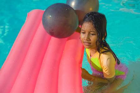 lifestyle outdoors portrait of young happy and cute female child having fun with inflatable airbed in holidays resort swimming pool smiling carefree and cheerful in young girl vacations conceptの写真素材