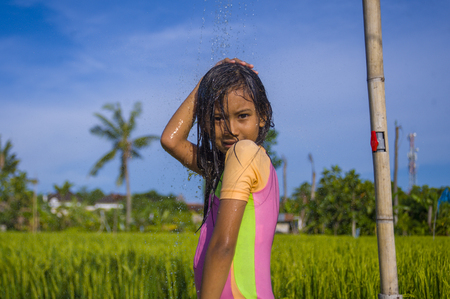 young happy and carefree beautiful child 7 or 8 years old outdoors having shower at a beautiful rice terrace playful under the water wearing cute girl swimsuit enjoying holidays and nature freeの写真素材
