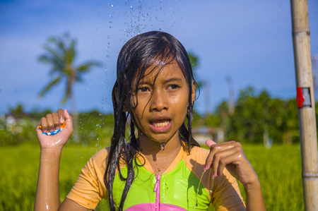 young happy and carefree beautiful child 7 or 8 years old outdoors having shower at a beautiful rice terrace playful under the water wearing cute girl swimsuit enjoying holidays and nature freeの写真素材
