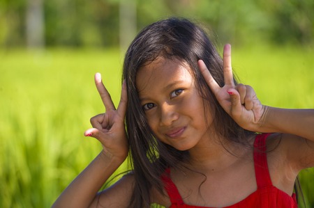 sweet happy and beautiful 7 or 8 years old child in cute red dress having fun posing outdoors smiling cheerful at rice field in young girl enjoying holidays and nature conceptの写真素材