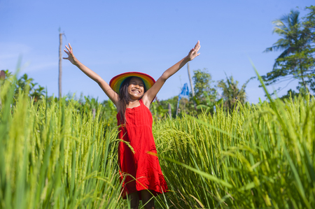 sweet happy and beautiful 7 or 8 years old child in Summer hat and cute red dress having fun outdoors smiling cheerful at rice field in young girl enjoying holidays conceptの写真素材