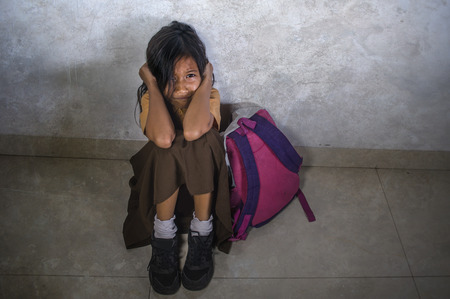 dramatic portrait of sad and depressed 8 or 9 years old child in school uniform sitting on the floor with her bad crying helpless feeling scared and desperate suffering bullying and abuseの写真素材