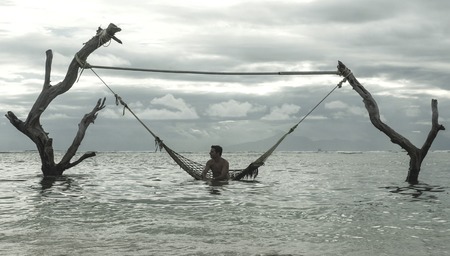 man lying relaxed and happy in sea hammock amazing set up on tree trunks at tropical island beach in...