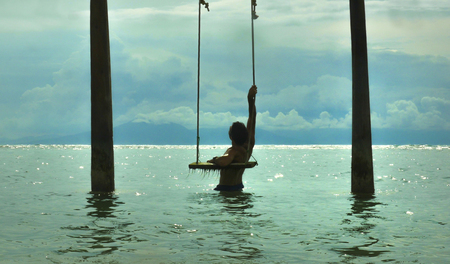 young fit and attractive man enjoying Summer holidays sitting on sea swing at tropical island beach...