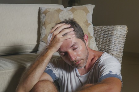 lifestyle portrait young attractive sad and depressed man sitting on living room floor feeling...