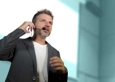 young attractive and confident successful man with headset speaking at corporate business coaching and training auditorium conference room talking giving motivation training from speaker stageの写真素材