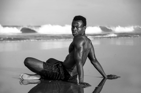 summer holidays lifestyle portrait of young attractive and relaxed afro American man with fit body and muscular back sitting on beach sand posing cool badass attitude in black and whiteの写真素材