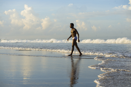 young attractive and sexy black afro American man with sexy muscular body walking on beautiful tropical desert beach enjoying Summer holidays free and relaxed in beauty and wellness conceptの写真素材