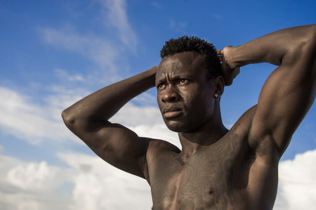 close up head and shoulders portrait of young attractive and fit black afro American man with strong muscular body posing cool model attitude on the beach isolated on Summer blue skyの写真素材