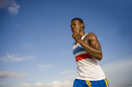 healthy lifestyle portrait of young athletic and attractive black African American runner man doing running workout training on desert beach in fitness and wellness isolated on blue skyの写真素材