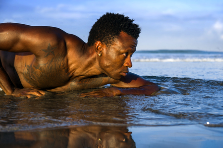 artistic expressive portrait of young attractive and sexy black afro American man with athletic muscular body posing cool in sea water on desert beach in male beauty and plasticity conceptの写真素材
