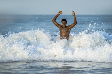 lifestyle desert beach portrait of young fit and attractive black African American man with muscular beautiful body enjoying playful in the sea playing on the water having fun in Summer holidaysの写真素材