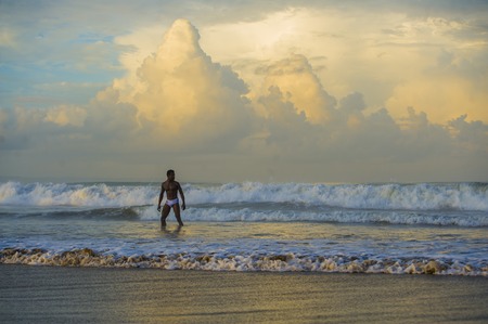 artistic portrait of young attractive and fit black African American man with sexy muscular body carefree enjoying nature feeling free on beach in wild sea with big waves in beauty and healthの写真素材