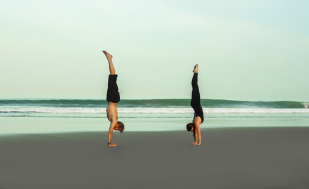 young attractive and beautiful acrobat couple practicing acroyoga exercise concentrated keeping balance practiing yoga on the beach in relaxation and meditation concept and healthy lifestyleの写真素材