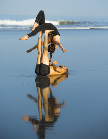 young attractive and beautiful acrobat couple practicing acroyoga exercise concentrated keeping balance practicing yoga on the beach in relaxation and meditation concept and healthy lifestyleの写真素材
