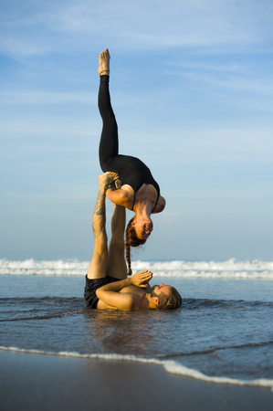 young attractive and beautiful acrobat couple practicing acroyoga exercise concentrated keeping balance practicing yoga on the beach in relaxation and meditation concept and healthy lifestyleの写真素材