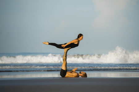 young attractive and beautiful acrobat couple practicing acroyoga exercise concentrated keeping balance practicing yoga on the beach in relaxation and meditation concept and healthy lifestyleの写真素材