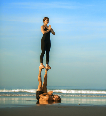 young attractive and beautiful acrobat couple practicing acroyoga exercise concentrated keeping balance practicing yoga on the beach in relaxation and meditation concept and healthy lifestyleの写真素材