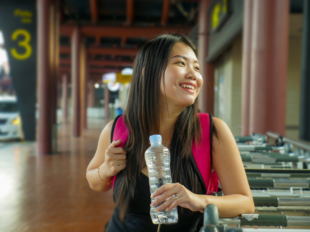 lifestyle portrait of young happy and attractive Asian Korean woman with backpack smiling excited and playful at airport arrival or departure in holidays travel fun and millennial backpacker conceptの写真素材