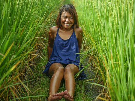 natural and fresh portrait of young happy and exotic islander Asian girl from Indonesia smiling cheerful and excited posing in green field playing with rice enjoying holidays tripの写真素材