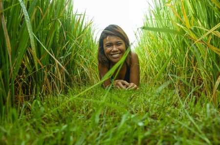 natural and fresh portrait of young happy and exotic islander Asian girl from Indonesia smiling cheerful and excited posing in green field playing with rice enjoying holidays tripの写真素材