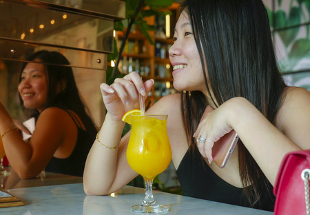 young happy and relaxed Asian Korean tourist woman drinking healthy orance juice at hotel cafe or restaurant resort smiling cheerful in tourism travel and lifestyle conceptの写真素材