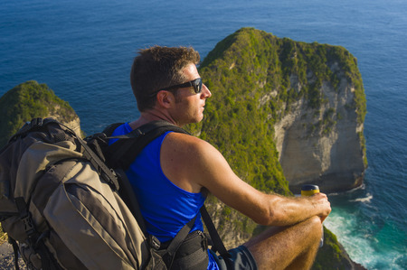 lifestyle outdoors portrait of young attractive and handsome man with backpack trekking beach cliff looking at beautiful sea landscape in sport adventure and summer holidays getawayの写真素材