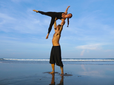 healthy and attractive fit couple of acrobats  doing acroyoga balance and meditation exercise on beautiful desert beach practicing balance and harmony posing in healthy lifestyle and yoga conceptの写真素材