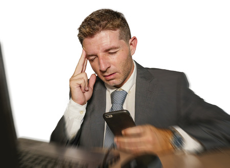 young frustrated and stressed businessman in suit and tie working overwhelmed at office laptop computer desk suffering headache cause of work stress isolated on white backgroundの写真素材