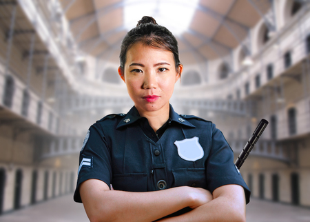 portrait of young serious and attractive Asian American guard woman standing at State penitentiary prison hall wearing police uniform in crime punishment and law enforcement conceptの写真素材