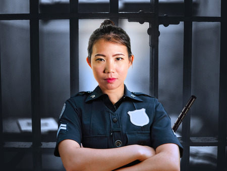 portrait of young serious and attractive Asian Chinese guard woman standing on cell at State penitentiary wearing police uniform in crime prison punishment and law enforcement conceptの写真素材