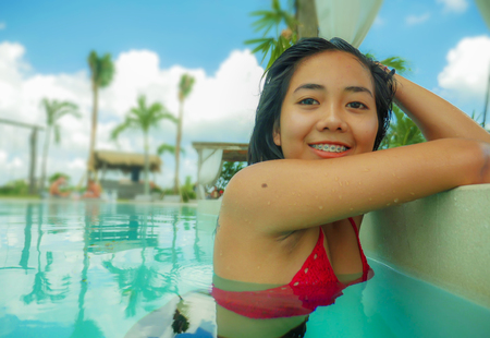 outdoors portrait of young beautiful and sweet Asian Indonesian teenager girl swimming at tropical...
