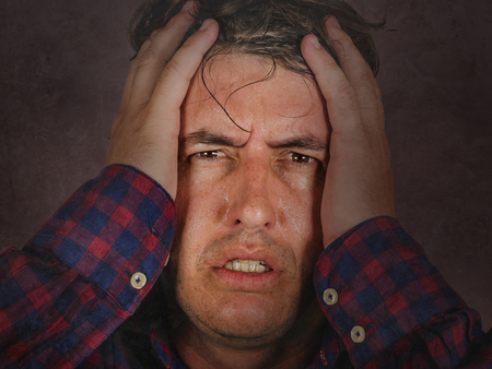 close up dramatic portrait of stressed and overwhelmed man holding head with hands in crazy stress and frustrated face expression looking to camera having problem isolated white backgroundの写真素材
