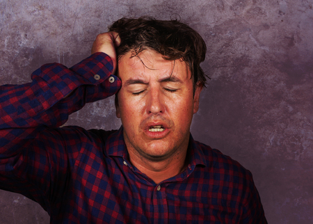 dramatic portrait of stressed and overwhelmed white man holding head with hands in crazy stress and frustrated face expression looking to camera having problem isolated on grunge backgroundの写真素材