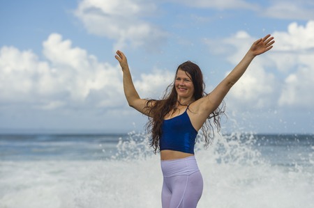 young happy and attractive red hair woman playing excited spreading arms feeling free and relaxed getting wet by sea waves splashing on her enjoying beach holidays trip and healthy lifestyleの写真素材