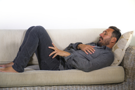 lifestyle home portrait of young attractive and happy white man with beard and casual shirt lying relaxed and cozy at living room sofa couch resting and smiling cheerfulの写真素材